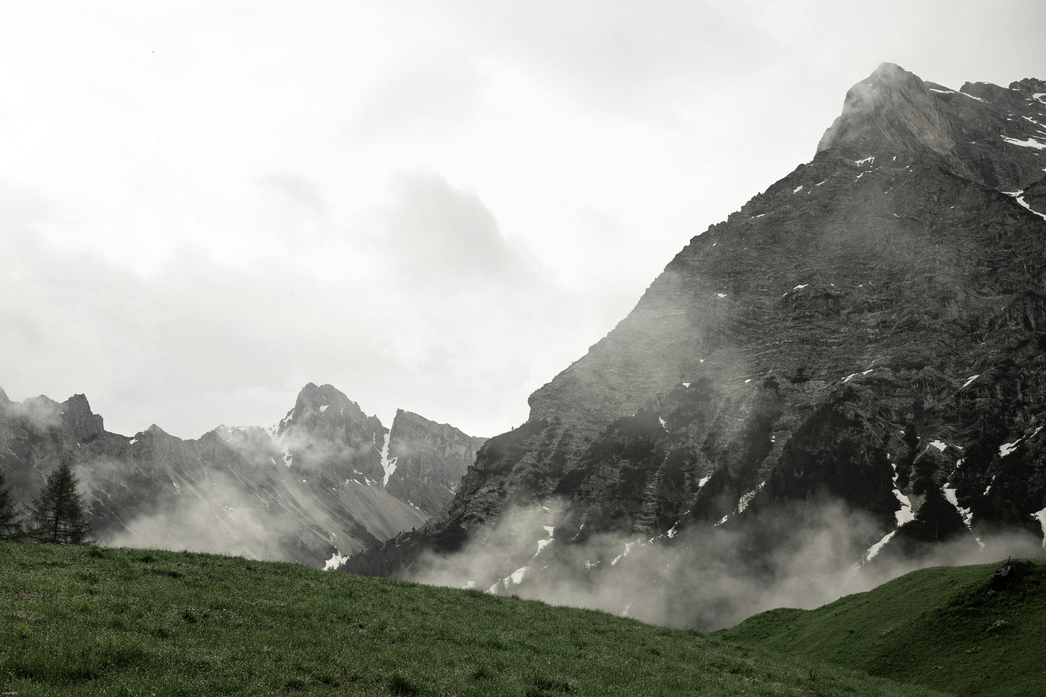 Severe mountains near grassy foggy lawn